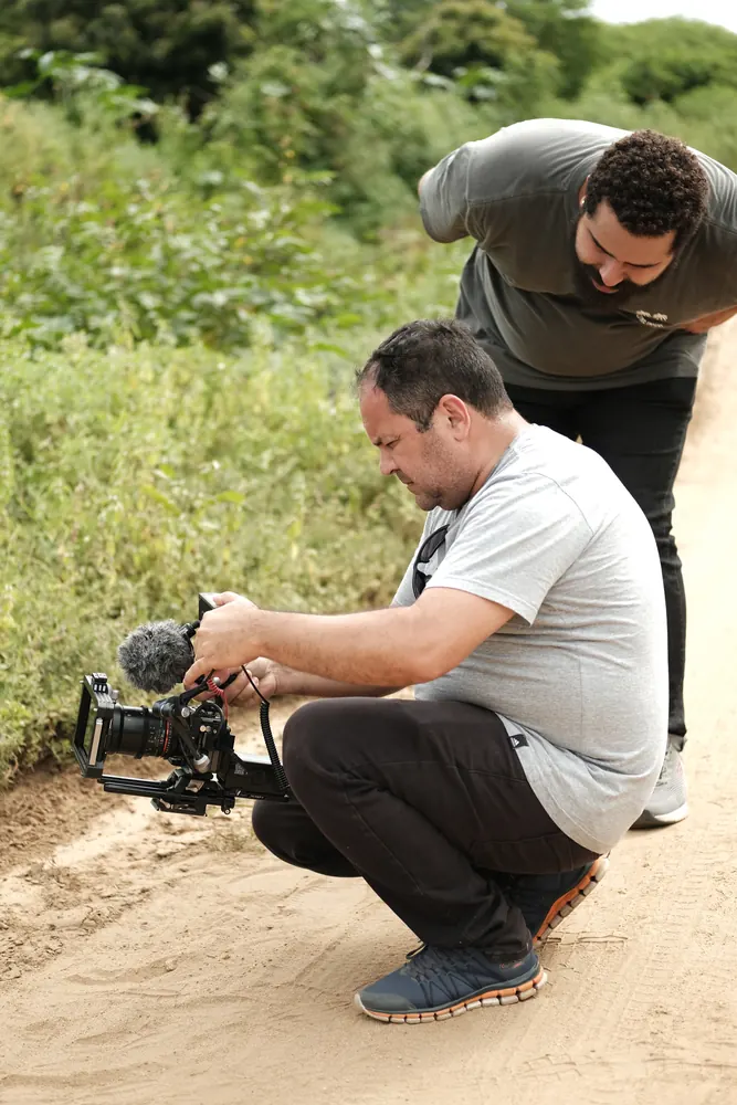 Cinegrafista agachado filmando em estrada de terra.