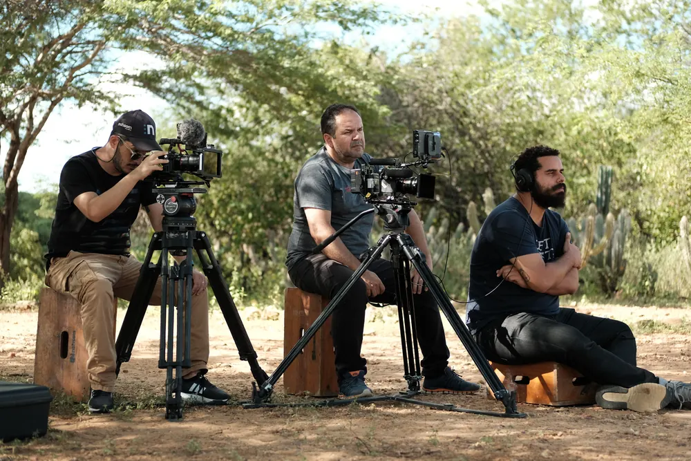 Equipe com câmeras em tripés filmando ao ar livre.